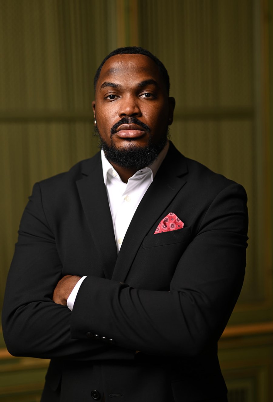 Nicholas Smith in a black suit and white shirt with a red pocket square, arms crossed